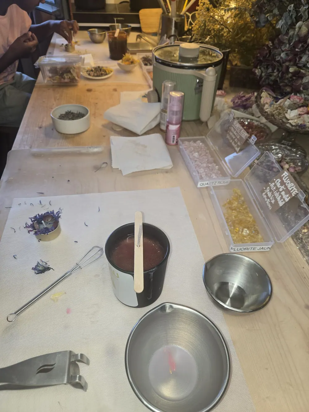 L'atelier en cours : la cire fondue prête à couler, les fleurs séchées et les pierres à choisir.